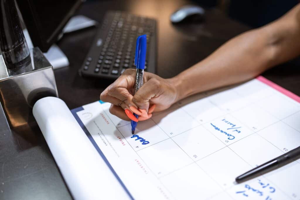 person writing on desk calendar to track business day deadlines showing does saturday count as a business day