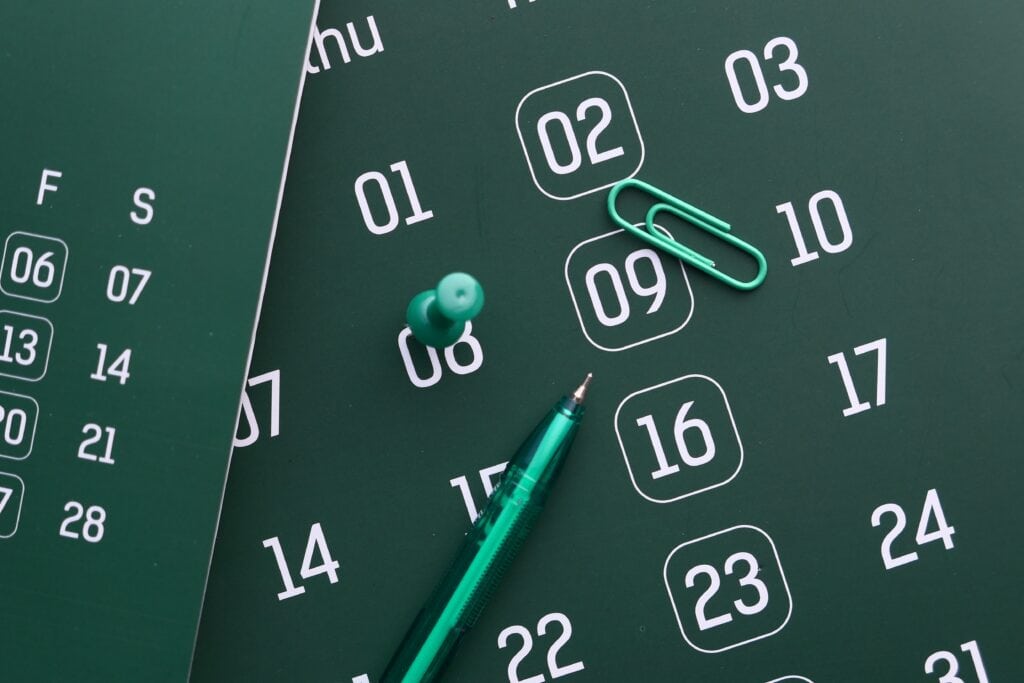 Green calendar with pen and paperclip used to subtract business days from a date and count back to a deadline